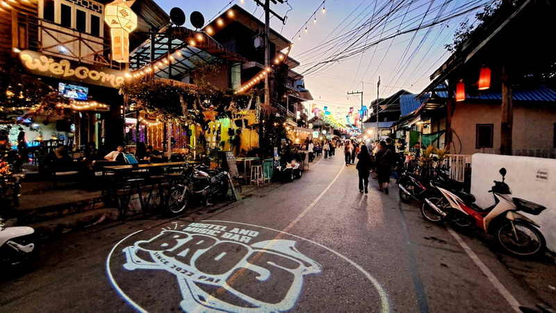 Street scene with shops, motorcycles, and people walking at dusk with string lights overhead at Pai Walking Street.