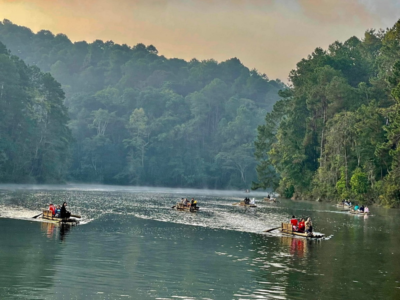 Boats with people sailing on a misty river surrounded by lush forest at Pang Ung.