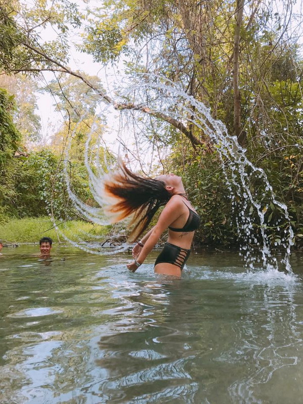 River Scene with People at Sai Ngam Hot Spring Woman flipping her hair in a river surrounded by trees with a man swimming nearby at Sai Ngam Hot Spring.