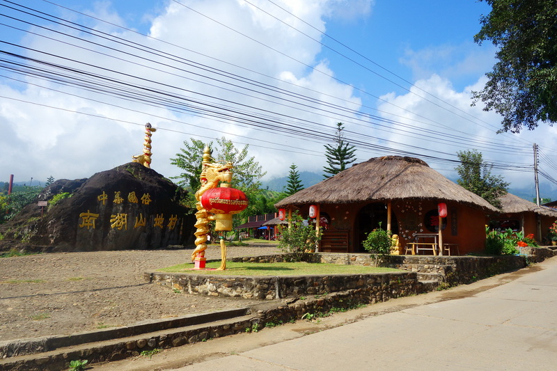 Traditional hut with dragon statue and large engraved rock surrounded by trees at Santichon Village.