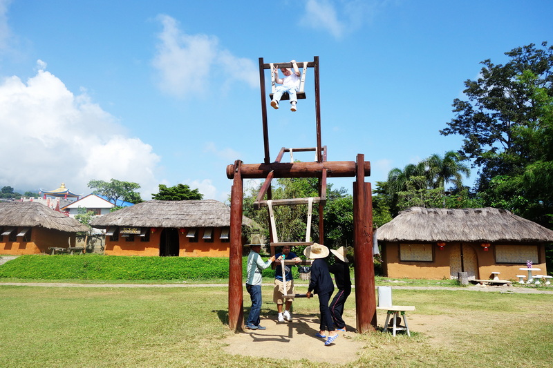 People playing on a large wooden swingset outdoors under a clear blue sky at Santichon Village.