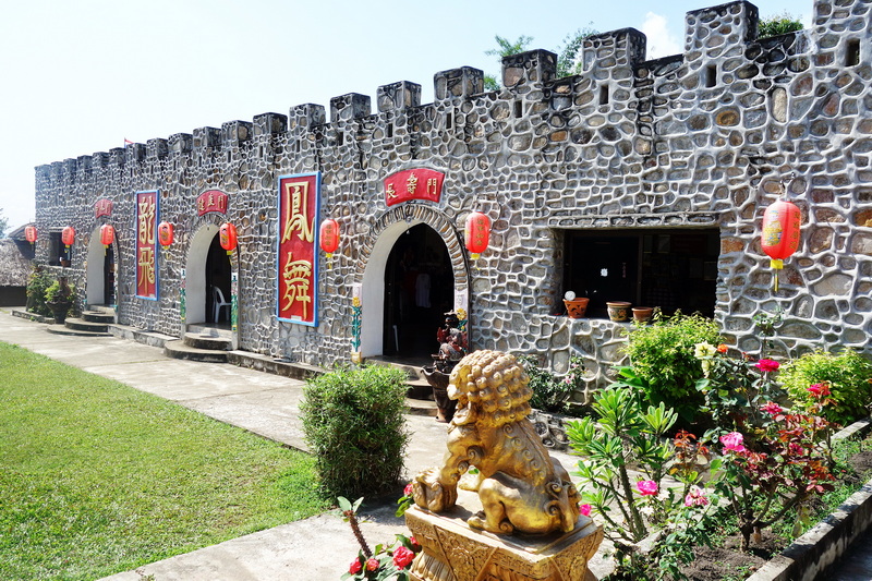 Stone building with arched doorways, red lanterns, and surrounding flower bed at Santichon Village.