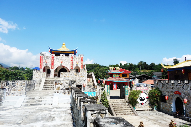 Traditional Chinese-style temple entrance with colorful roofs and stone stairs under a blue sky at Santichon Village.