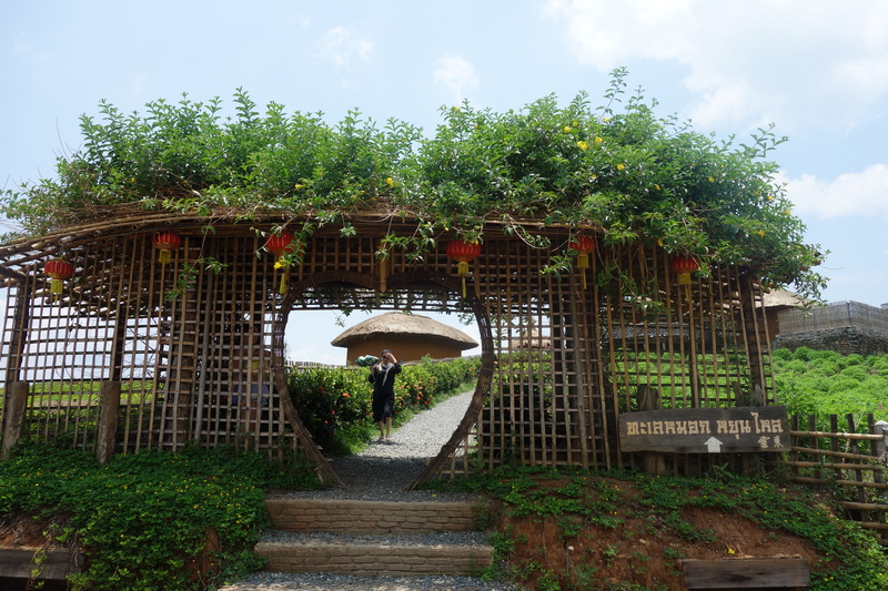 Wooden archway overgrown with greenery and hanging red lanterns, leading into a garden area at Mae Hong Son.