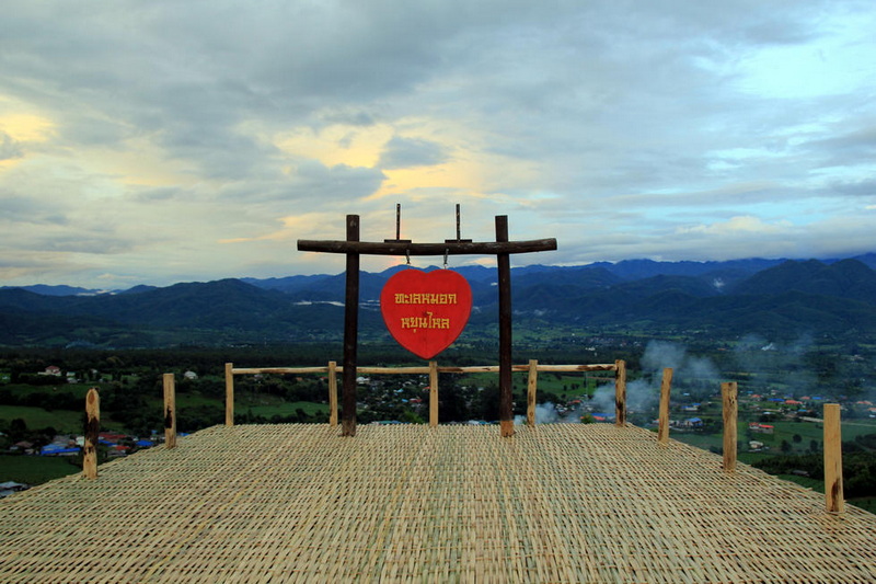 Wooden platform with heart-shaped sign overlooking a valley and mountains under clouds at Santichon Village.