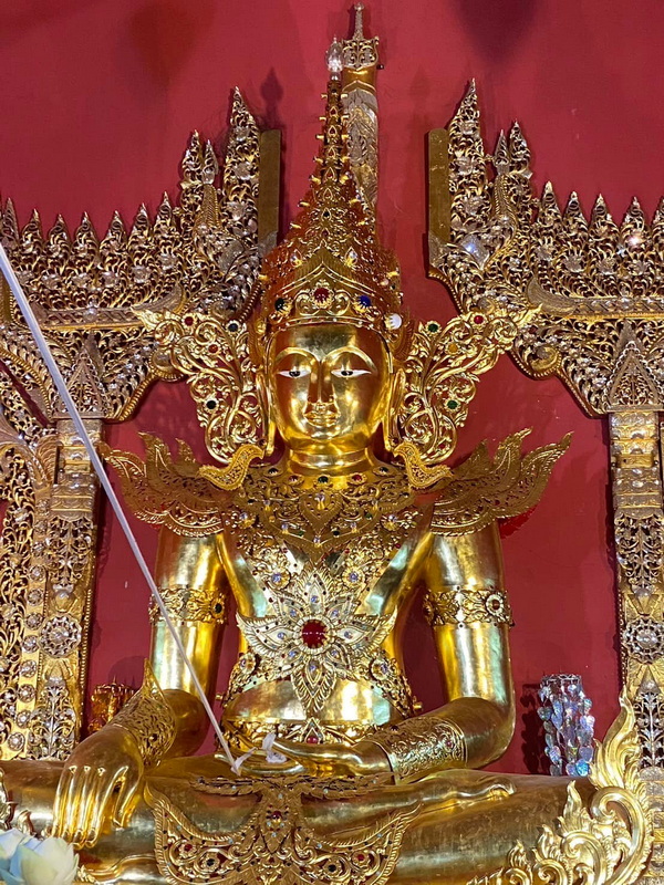 Gold-colored deity statue with ornate decorations and jewelry against a red wall at Su Tong Pae Bridge.