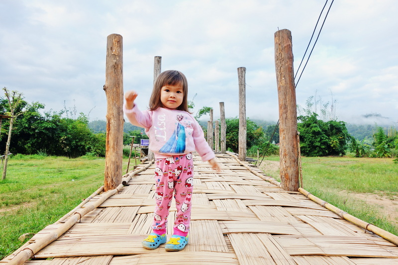 Girl standing on a wooden bridge in a grassy, tree-filled landscape at Su Tong Pae Bridge.