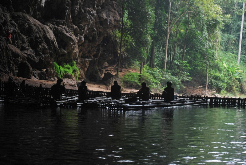 Inside Tham Lod Cave People sitting on a bamboo raft inside a dark cave with greenery outside at Tham Lod.
