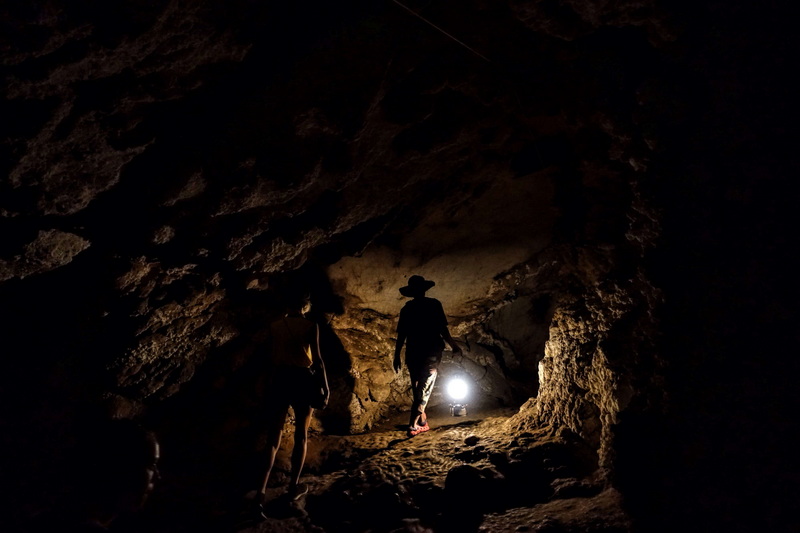 Two explorers inside a dark cave with a flashlight illuminating rocky walls at Tham Lod.