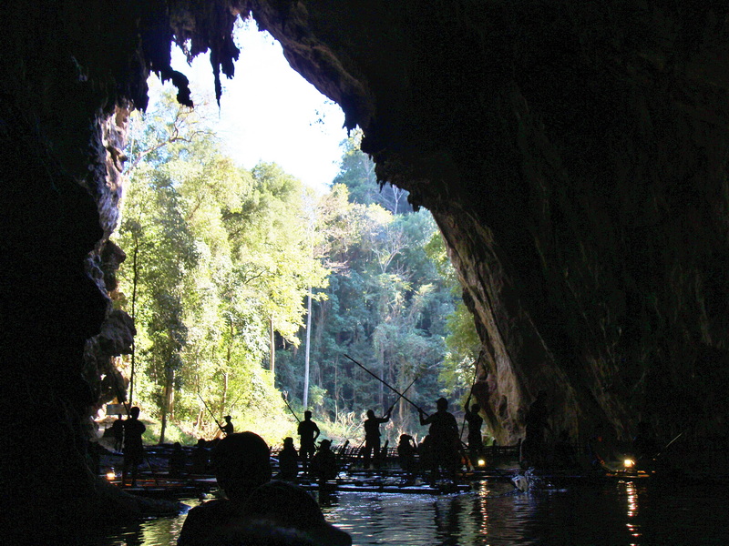 People fishing inside a dark cave with an opening to a forest outside at Tham Lod Cave.