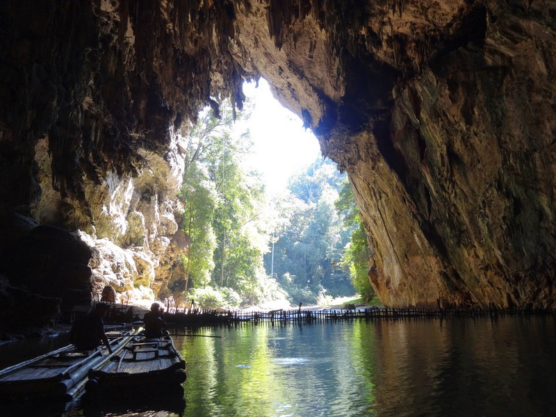 Inside a cave with boats on water and sunlight streaming through the entrance at Tham Lod.