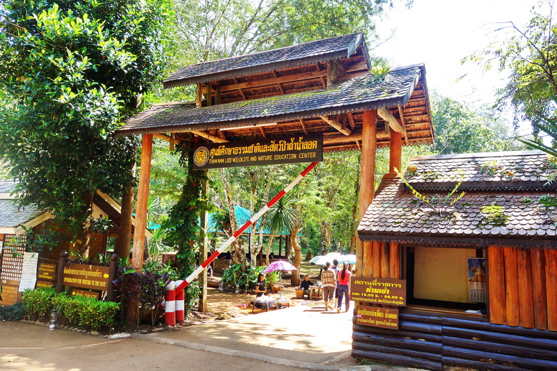 Wooden entrance gate with sign, trees, and visitors at Tham Lod Cave in Mae Hong Son.