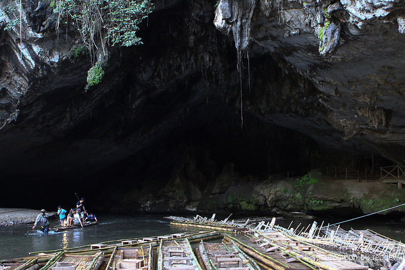 Cave Entrance with Bamboo Rafts at Tham Lod People riding bamboo rafts at the entrance of a large dark cave with rocky overhangs at Tham Lod.