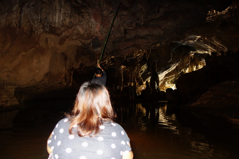 Exploring a Cave Interior at Tham Lod Cave Person wading through a dark cave with stalactites and water reflections at Tham Lod Cave.