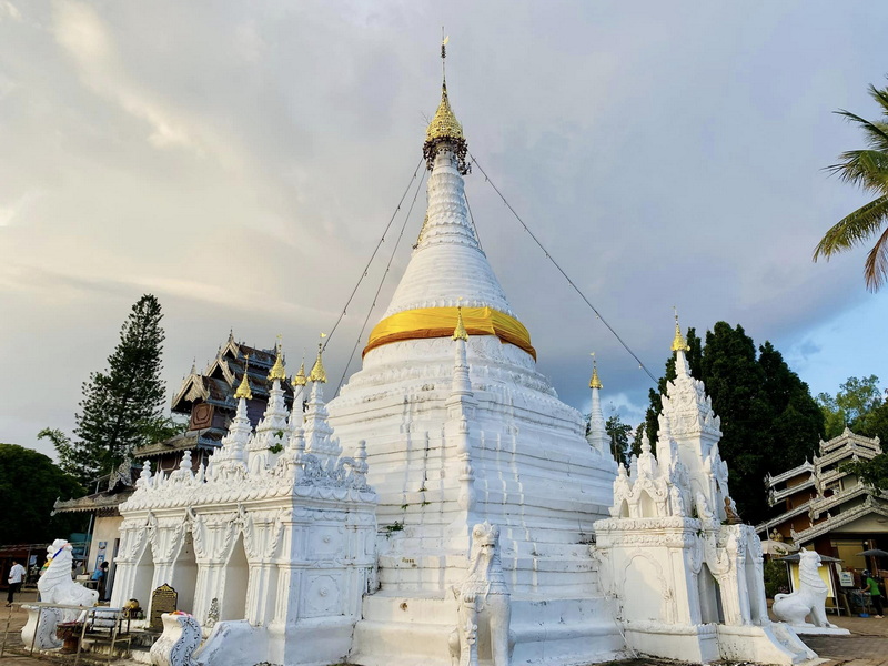 White pagoda with golden ring and detailed carvings amidst surrounding temples and trees at Wat Phra That Doi Kong Mu.