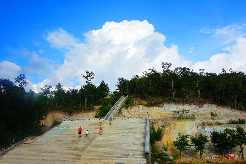 People walking up a large outdoor staircase surrounded by greenery under a clear sky at Wat Phra That Mae Yen.