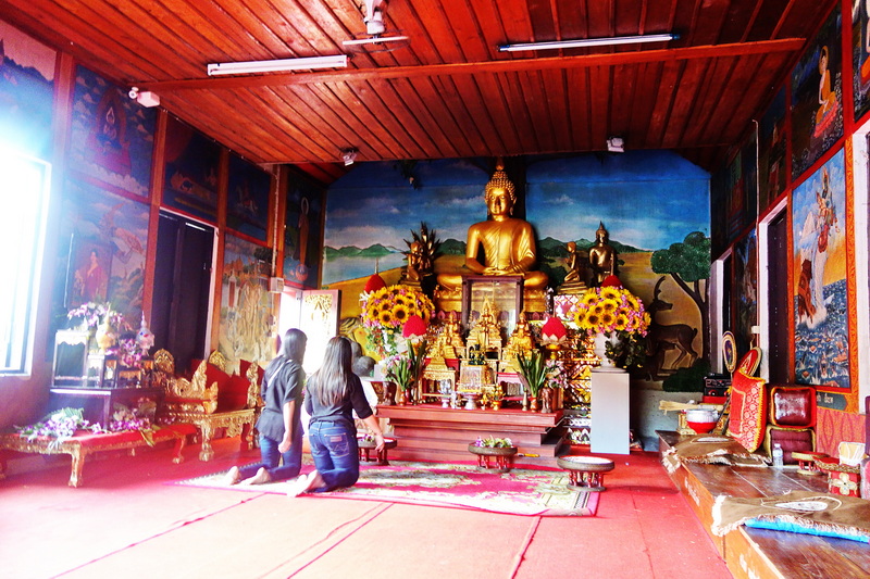 People kneeling before a large golden Buddha in a decorated temple room at Wat Phra That Mae Yen.