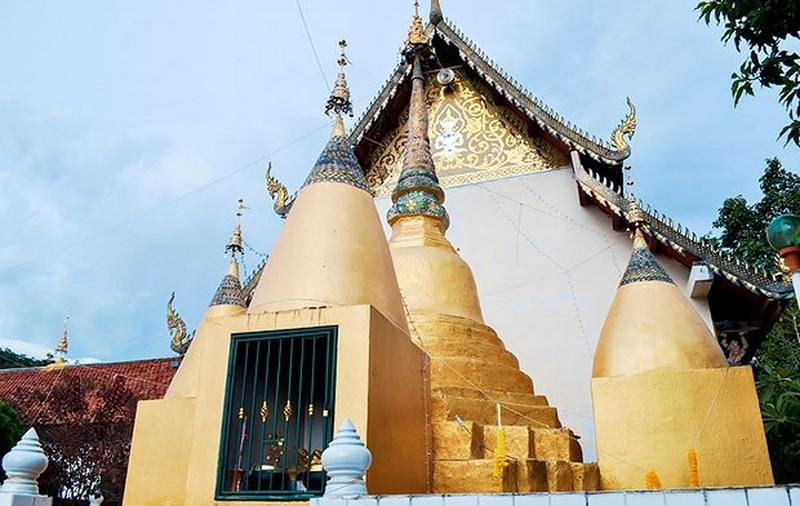 Golden temple with spires and ornate details under a blue sky at Wat Phra That Mae Yen.