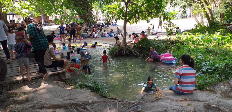 River Play Area Scene at Bua Tong Sticky Waterfall People of all ages enjoy swimming and playing in a shallow river under trees at Bua Tong Sticky Waterfall.