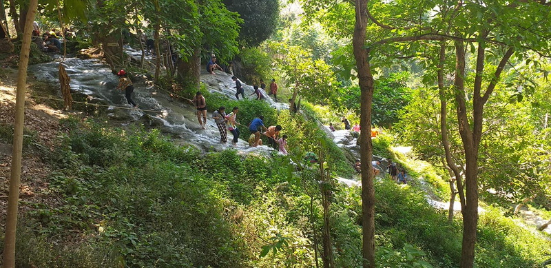 People exploring a water-covered slope amidst lush green trees and forest at Buatong Waterfall.