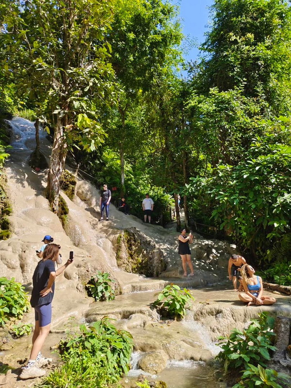 Tourists enjoy the limestone terraces and water flow amidst lush greenery at the waterfall at Bua Tong Sticky Waterfall.