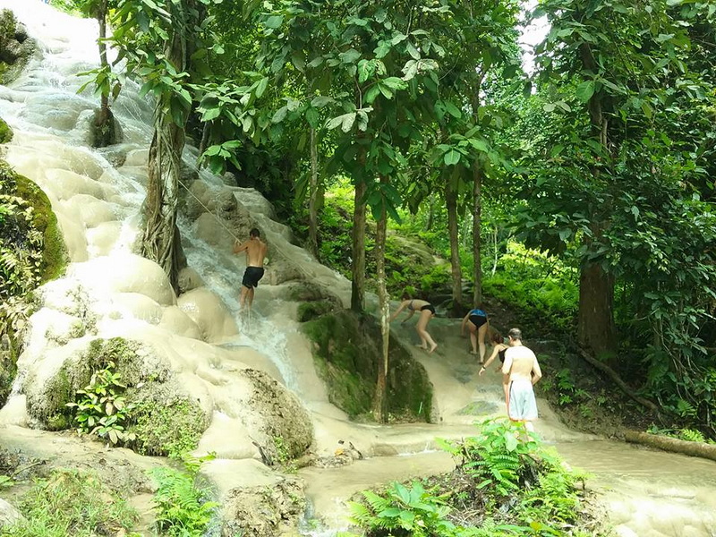 People climbing and playing on a mineral-rich waterfall surrounded by dense greenery at Buatong Waterfall.