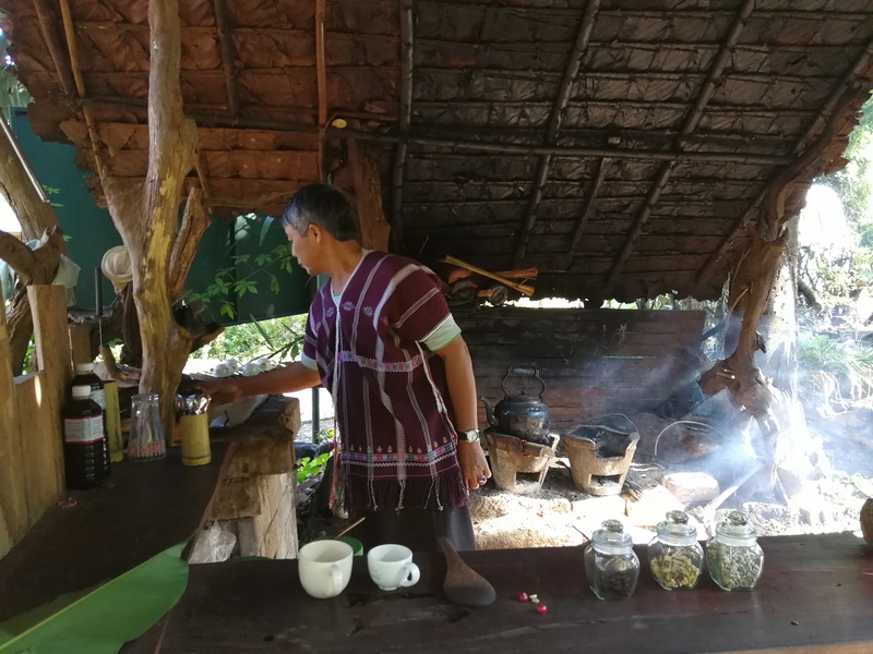 Traditional Tea Preparation at Doi Inthanon National Park Person in traditional attire preparing a drink inside a rustic open-sided hut with jars and kitchenware at Doi Inthanon National Park.