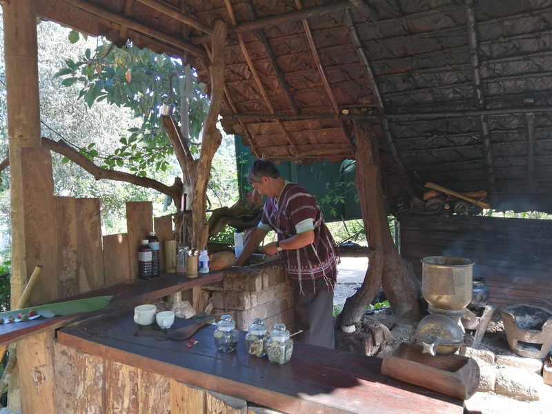 Traditional Food Preparation Scene at Mae Klang Luang Village Person preparing food under a thatched roof shelter with trees and greenery around at Mae Klang Luang Village.
