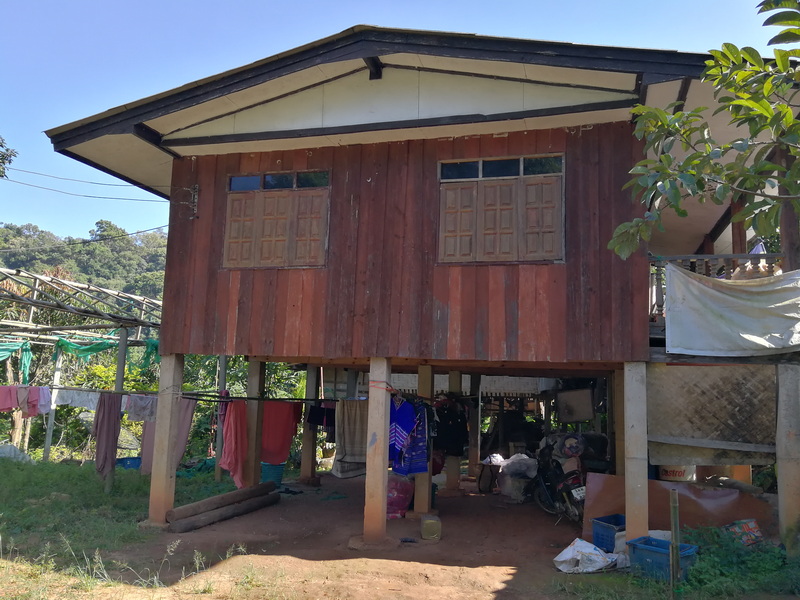Stilt house with windows and laundry outside, surrounded by greenery at Ban Mae Klang Luang.