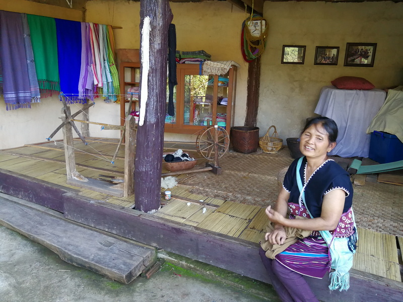 Traditional Interior Scene at Mae Klang Luang Village A smiling woman sitting inside a rustic room with colorful fabrics on the wall at Mae Klang Luang Village.