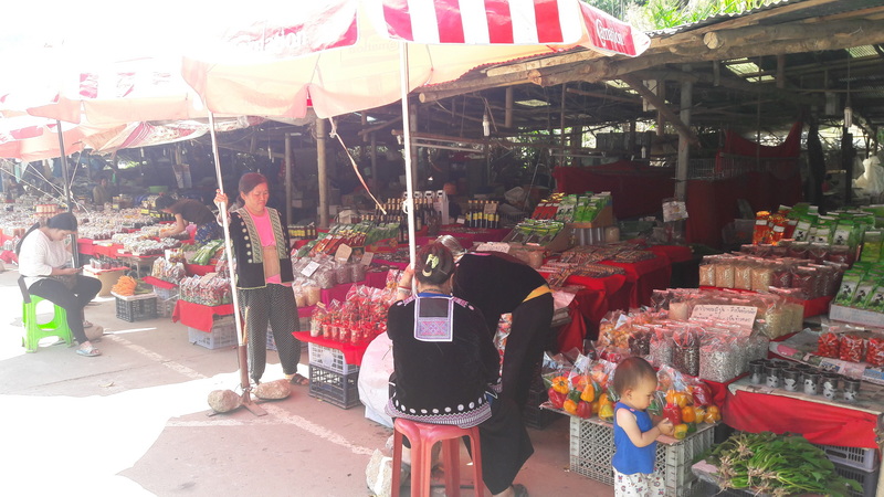 People shopping at an outdoor market with colorful stalls and umbrellas at Doi Inthanon Hmong Market.