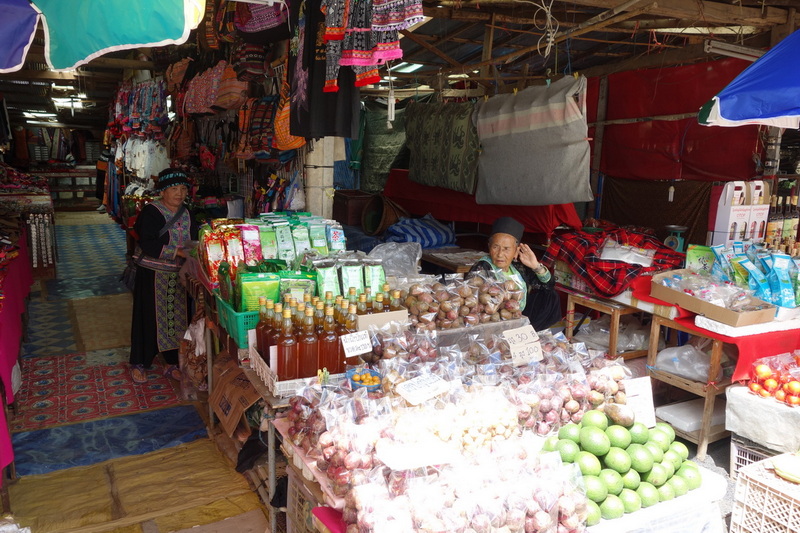 Market stall with bottled liquids, onions, and colorful tarps in a local market setting at Doi Inthanon Hmong Market.
