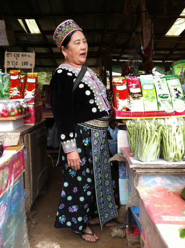 Woman in traditional dress inside market with packaged goods and vegetables at Doi Inthanon Hmong Market.