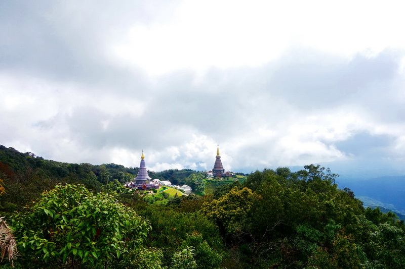 View of two pagoda temples on a green hilltop surrounded by mountains and trees at Kew Mae Pan Nature Trail.
