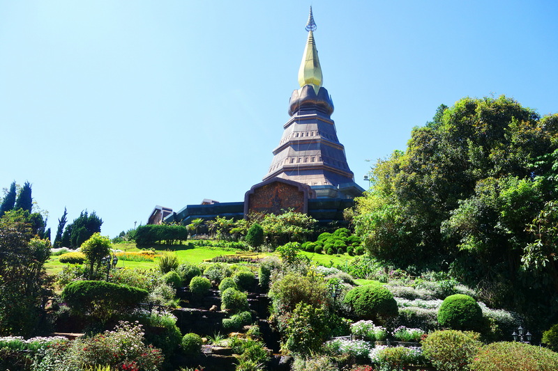 Tall pagoda with a golden spire standing amidst lush gardens and bushes at King and Queen Pagodas.