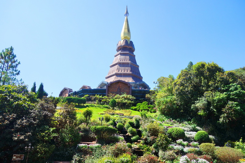 Tall pagoda with multiple tiers and a pointed spire against a bright blue sky, surrounded by greenery at King and Queen Pagodas Doi Inthanon.