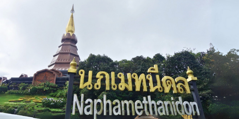 Sign with Thai and English text in front of a pagoda and temple grounds at King and Queen Pagodas.