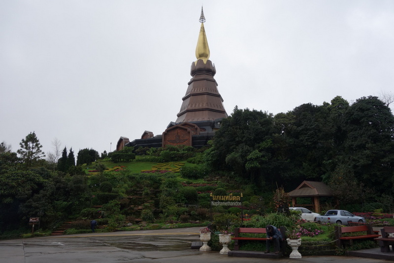 Tall golden spire monument atop a green hill with surrounding gardens and trees at Doi Inthanon National Park.