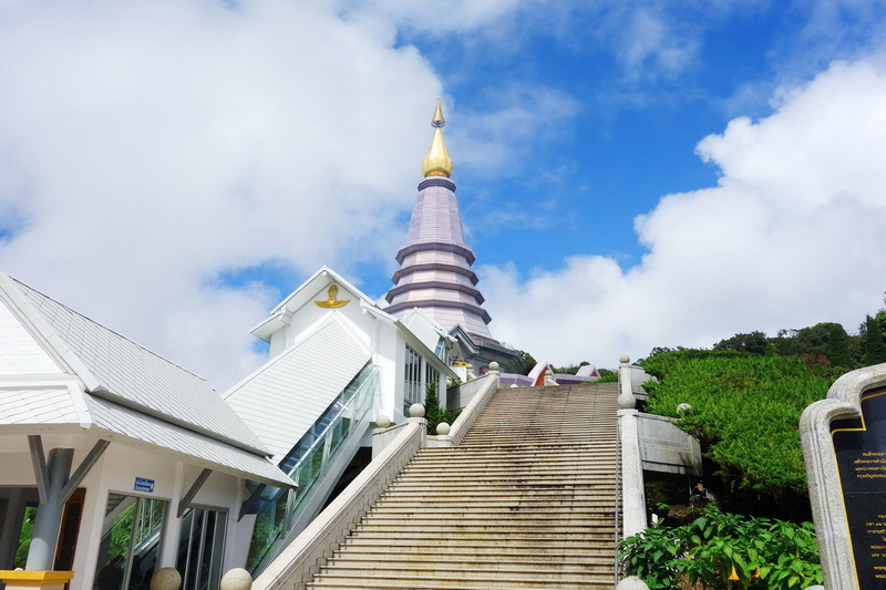 White temple with a tall spire against a blue sky and lush greenery at King and Queen Pagodas.