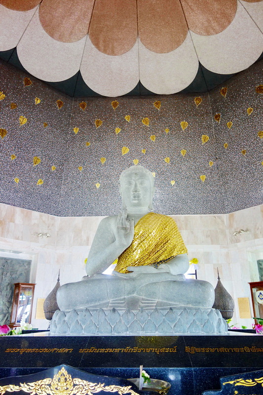 Seated Buddha statue with a golden shawl inside a temple with decorative ceiling patterns at King and Queen Pagodas Doi Inthanon.