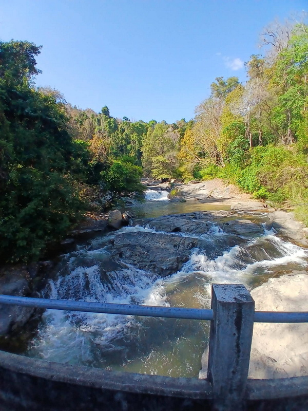 Scenic River in Forest at Mae Klang Waterfall River flowing over rocks surrounded by lush trees under a blue sky at Mae Klang Waterfall.