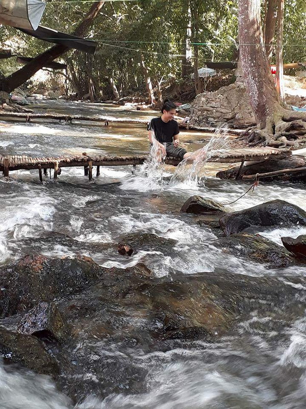 Stream in Forested Area at National Parks in Chiang Mai Person sitting on a wooden platform in a flowing stream surrounded by trees and rocks at National Parks in Chiang Mai.
