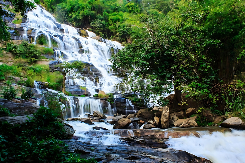 Scenic Waterfall in Nature at Mae Ya Waterfall Water cascading down rocks surrounded by lush green trees and foliage at Mae Ya Waterfall.