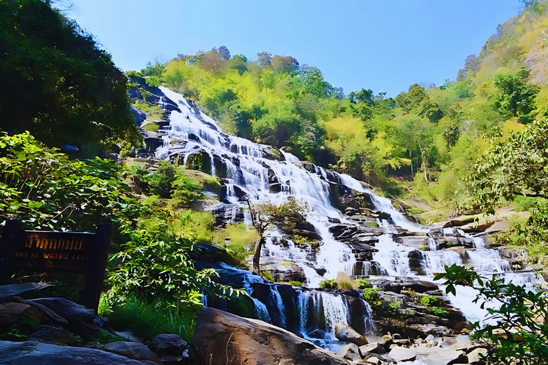 Scenic Waterfall in Nature at Mae Ya Waterfall A waterfall flowing down rocks surrounded by green trees on a sunny day at Mae Ya Waterfall.