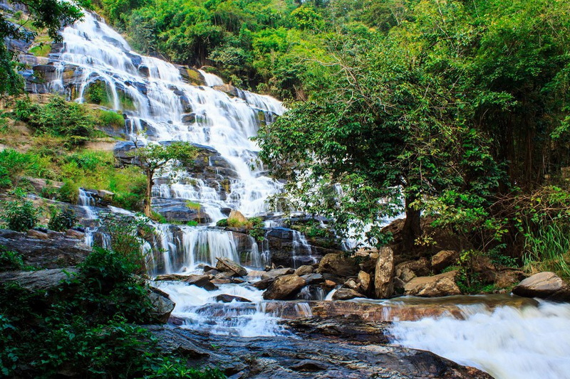Waterfall cascading over rocky ledges surrounded by lush trees and greenery at Mae Ya Waterfall.