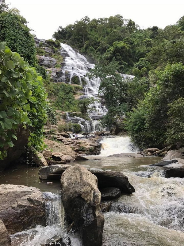 A scenic waterfall with multiple levels flowing over rocks surrounded by dense greenery at Doi Inthanon National Park.