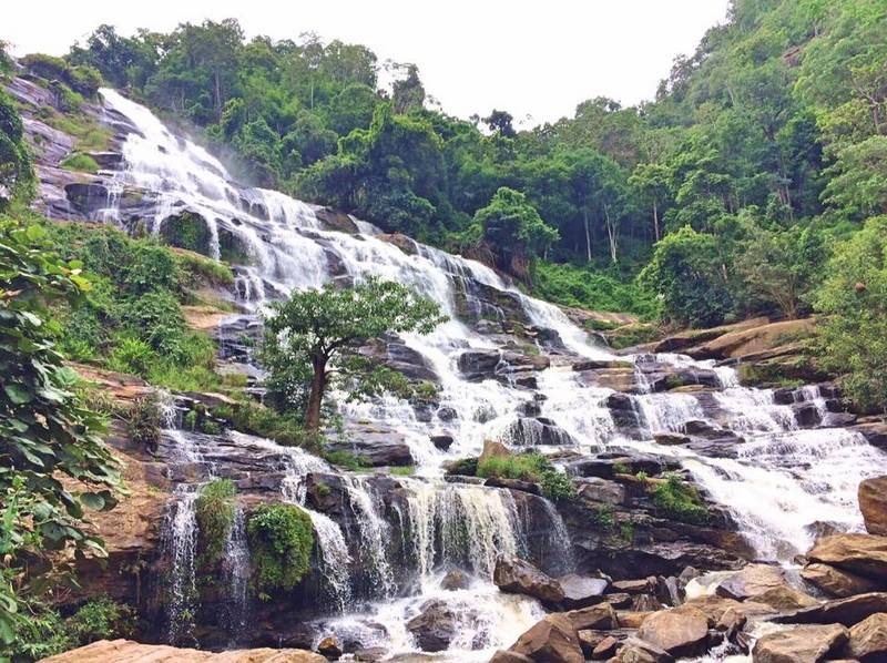 Scenic Waterfall in Lush Forest at Mae Ya Waterfall Water flows over rocks in a multi-tiered waterfall surrounded by green trees and plants at Mae Ya Waterfall.