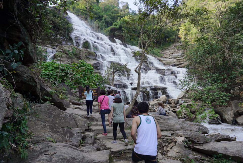 Hiking Near a Waterfall at Mae Ya Waterfall People hiking on rocks beside a waterfall surrounded by lush greenery at Mae Ya Waterfall.