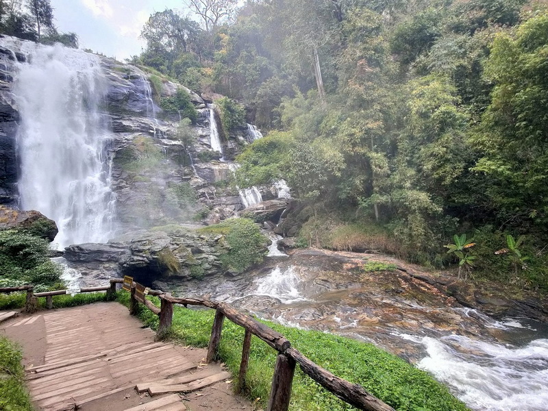 Scenic Waterfall and Nature Path at Wachirathan Waterfall Waterfall flowing over rocks with greenery and a wooden pathway in front at Wachirathan Waterfall.