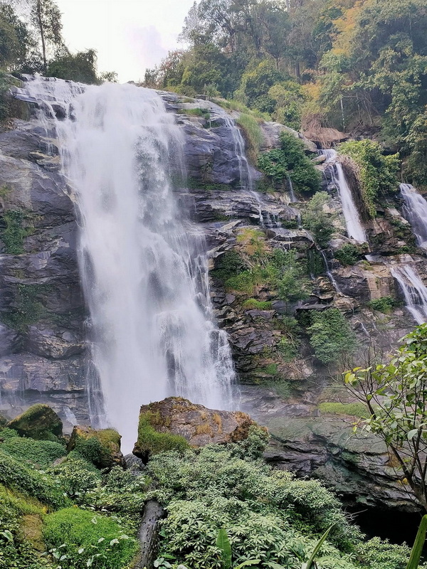 Tall waterfall cascading down a rocky cliff amidst lush green forest at Wachirathan Waterfall.
